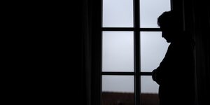 Ein Mann steht am Fenster seiner Wohnung.