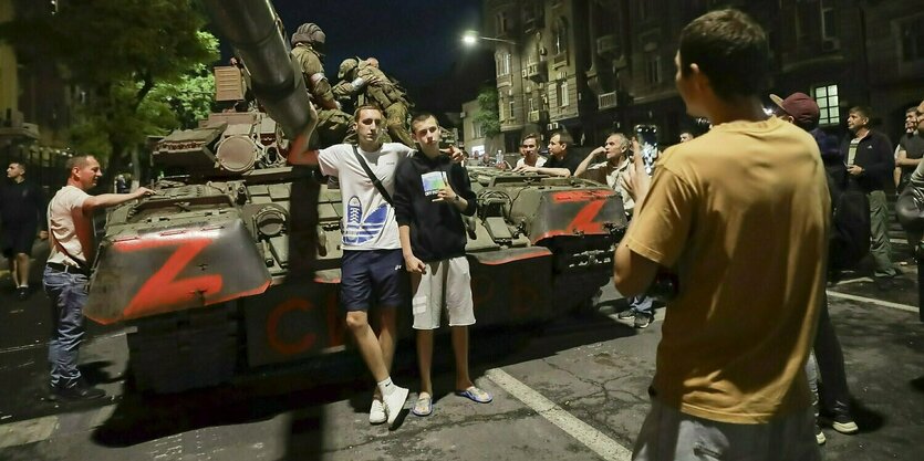 Zwei Männer in zivel posieren mit Soldaten vor einem Panzer, der mit den Buchstaben "z" bemalt ist