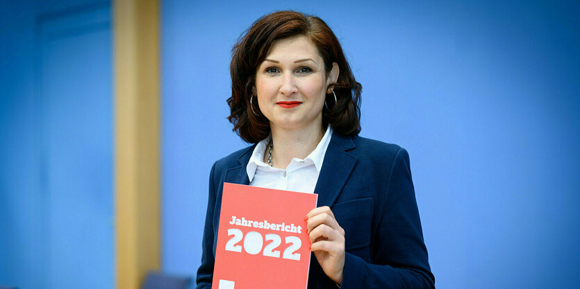 Ferda Ataman, eine Frau mit braunen, lockigen Haaren, hält den Jahresbericht der Antidiskriminierungsstelle in den Händen am 27. Juni 2023