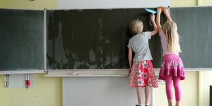 Zwei Kinder putzen eine Tafel