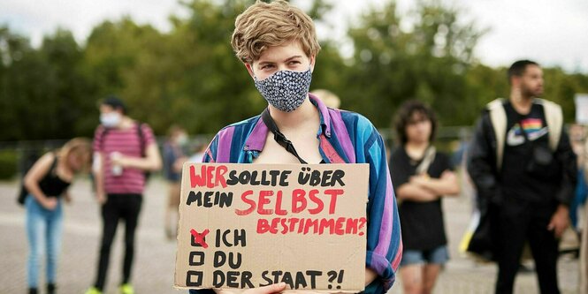 Ein Mensch hält ein Schild, darauf steht: "Wer sollte über mein SELBST bestimmen?" Darunter lässt sich ankreuzen: "Ich, Du, Der Staat". Bei "Ich" ist ein Kreuz gemacht