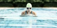 Eine junge Frau schwimmt in enem Schwimmbecken im Freibad und holt beim Brustschwimmen gerade Luft. Sie trägt eine Badekappe