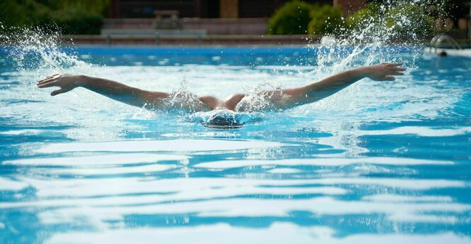 Ein Mann mit ausgebreiteten Armen schwimmt eine Bahn im Schmetterlingsstil