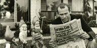 Günter Wallraff posiert mit Bild-Zeitung, im Hintergrund Gartenzwerge und ein Haus