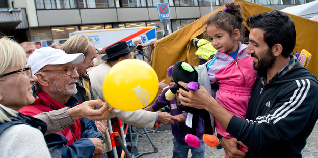 Flüchtling mit Tochter auf dem Arm wird ein Luftballon und ein Teddy erreicht