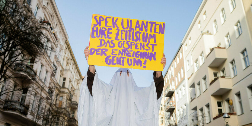 Eine als geist verkleidete Person hält ein Schild in die Höhe: "Spekulanten eure Zeit ist um. Das Gespenst der Enteignung het um."