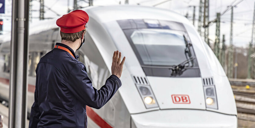 Ein Schaffner in Uniform steht vor einem Zug