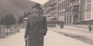 Alois Brunner mit Hut vor einer Häuserzeile