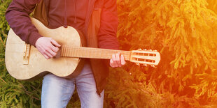 Ein Mann hält eine Gitarre in der Ansicht von den Füßen bis zum Hals