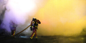 Ein Feuerwehrmann geht in eine dichte Rauchwand hinein, er trägt einen Schlauch auf seinen Schultern
