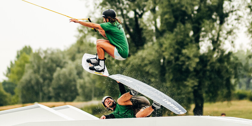 Zwei Wakeboarder praktizieren gemeisam einen Trick an einem Hindernis