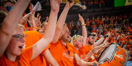 Fans in orangenen Trikots jubeln auf der Tribüne