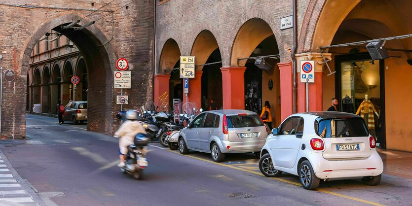 Parkende Autos vor Torbögen, an denen ein Motorroller vorbei fährt