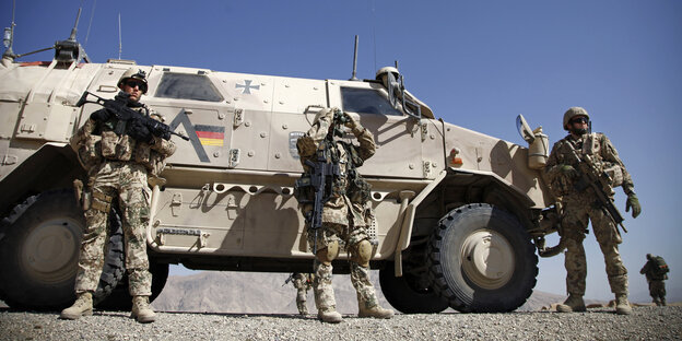 Drei Soldaten der Bundeswehr stehen vor einem gepanzerten Fahrzeug in einer wüstenähnlichen Umgebung