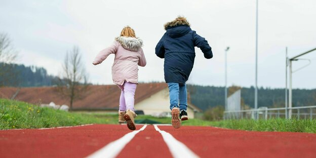 Zwei Kinder in dicken Jacken rennen auf einer Tartanbahn