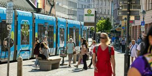 Straßenbahn fährt durch die Innenstadt in Augsburg, Menschen in Sommerkleidung unterwegs