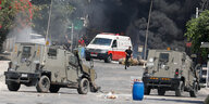 Militärlastwagen fahren auf der Straße, im Hintergrund schwarzer Rauch und junge Palästinenser unterwegs