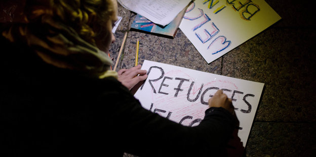 Eine Frau schreibt „Refugees welcome“ auf ein Schild