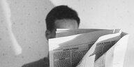 Mann versteckt sich lesend hinter der Zeitung
