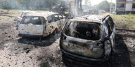 Zwei ausgebrannte Autos stehen vor Plattenbauten