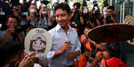 Pita Limjaroenrat steht in einem hellen Hemd vor Anhängern, im Hintergrund viele Fotografen