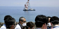 Eine Gruppe von Presseleuten im Vordergrund, im Hintergrund steht ein Schiff auf dem offenen Meer an der Küste Fukushimas