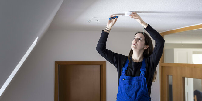 Das Bild zeigt eine junge Handwerkerin, die an einem Rauchmelder arbeitet.