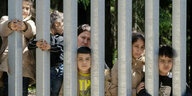 Eine Gruppe von Kindern und eine Frau stehen an einem Gitter