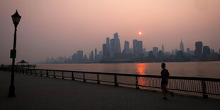 Ein Sonnenuntergang im Hintergrund, ein Fluss und eine Skyline sind im Hintergrund zu sehen, vorne eine Person am joggen