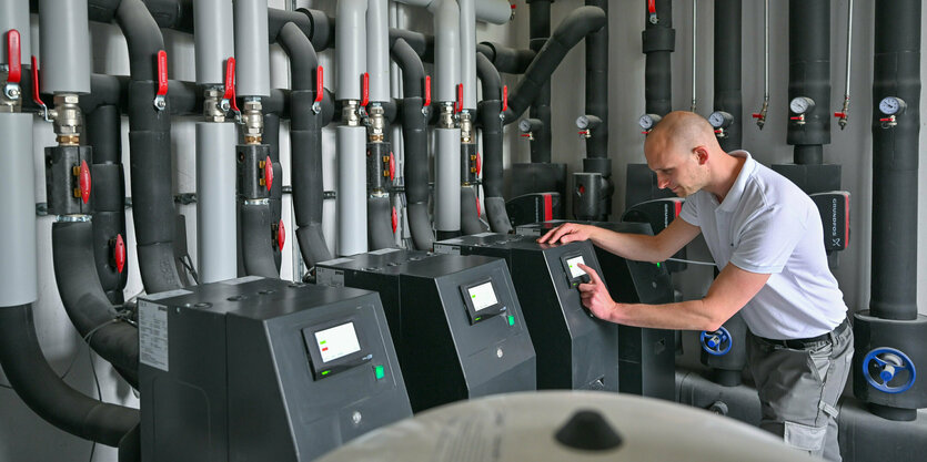 Ein Handwerker steht in einem Heizungsraum eines Altbaus mit mehreren modernen Sole-Wasser-Wärmepumpen.