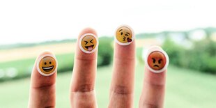 Auf den vier Fingerkuppen einer Hand kleben Smileys