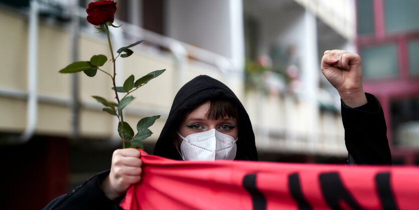 Frau mit gestreckter Faust und Rose in der Hand auf einer Demo gegen Femizide