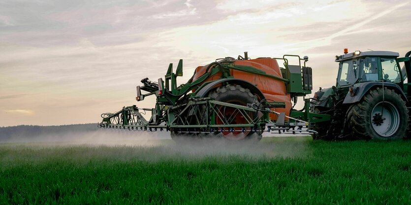 Ein landwirtschaftliches Gerät spritzt Pflanzenschutzmittel auf ein Feld mit grünen Pflanzen