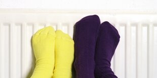 Kinderfüße in gelben und violetten Socken wärmen sich an einer Heizung