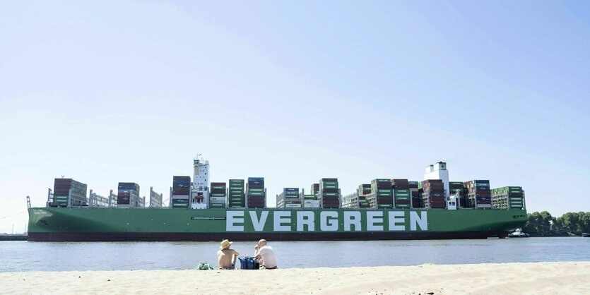 Zwei Menschen sitzen am Elbstrand und betrachten das große Containerschiff das vorbeifährt