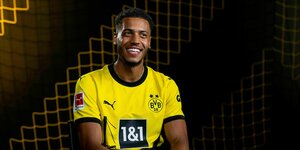 Felix Nmecha sitzt im Dortmundtrikot auf einer Bank und lacht