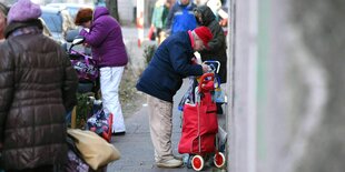 Menschen packen Lebensmittel der "Tafel" in ihre Taschen und Hackenporsche