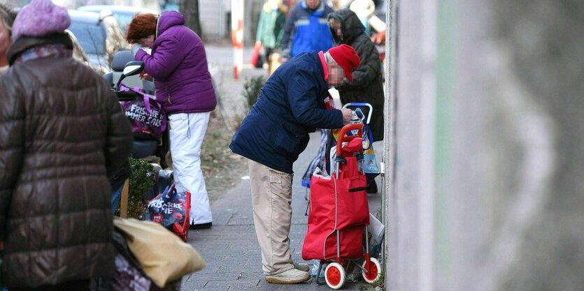 Menschen packen Lebensmittel der "Tafel" in ihre Taschen und Hackenporsche