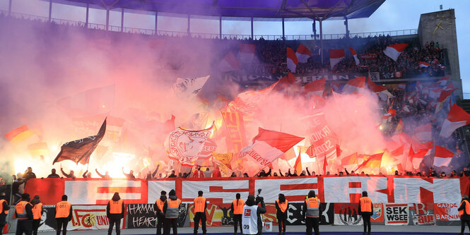 Fans von Union Berlin schwenken Fahnen und zünden Pyro im Gästeblock neben dem Marathontor.