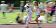 Zwei Mädchen rennen auf einer Tartanbahn, im Hintergrund Zuschauer - aber unscharf