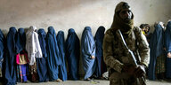 Ein Taliban steht vor Frauen die Schlange stehen und Burka tragen