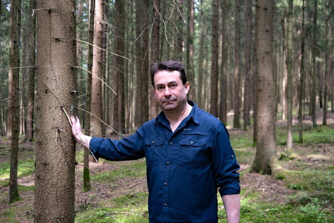 Portrait von Josef Ziegler, der in einem Wald an einem Baum lehnt