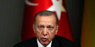 Erdogan spricht und sitzt vor einer Flagge der Türkei