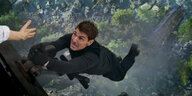 Tom Cruise hängt in der Luft, hält sich an einem offenem Flugzeug fest, jemand streckt seine Hand nach ihm aus