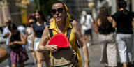 Eine ältere Frau geht durch die Hitze mit einem roten Fächer in der Hand