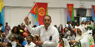 Ein Teilnehmer des Eritrea-Festivals in Gießen steht mit einer kleinen eritreischen Flagge zwischen den Stuhlreihen