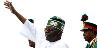 Nigerias Präsident in traditioneller weißer Kleidung winkt mit erhobenem Arm