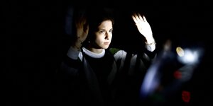Eine Klimaaktivistin hebt während einer Blockade die Hände - Nachtstimmung, nur ihr Gesicht und die Hand sind angeleuchtet