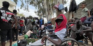 Migranten aus Afrika sitzen vor einem Gebäude der UNHCR in der Hitze, im Vordergrund sitzt ein Mann in einem Rollstuhl