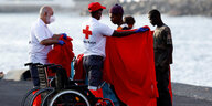 Retter geben einem geretteten Migranten eine rote Decke, sie haben auch Rollstühle an die Anlegestelle mitgebracht